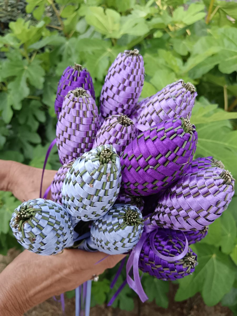 Bouquet de gros fuseaux de lavande tressés de satin bleu, lilas et violet, tenus à la main devant un feuillage