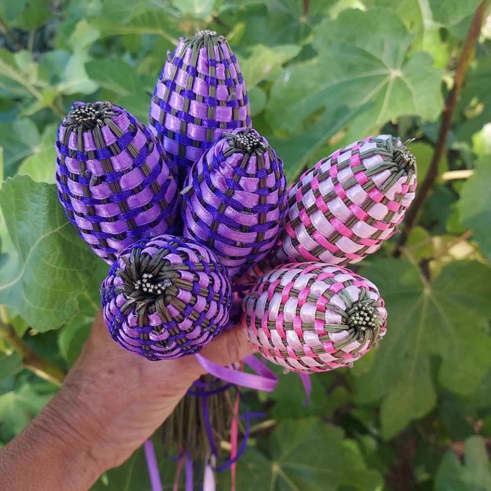Bouquet de fuseaux de lavande bicolores tressés de deux satins, violet et rose, tenus à la main devant un feuillage