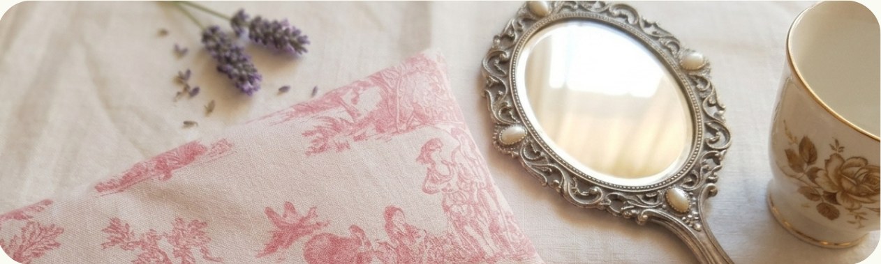Sachet de lavande à motifs romantiques posé sur du linge, avec une lavande séchée, un miroir ancien et une tasse